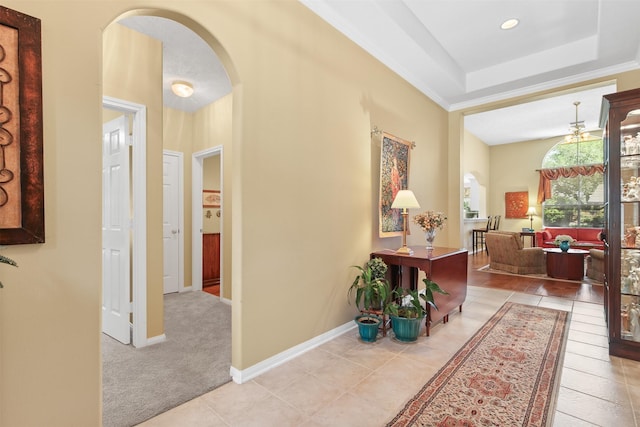 hall featuring arched walkways, tile patterned floors, baseboards, and a raised ceiling