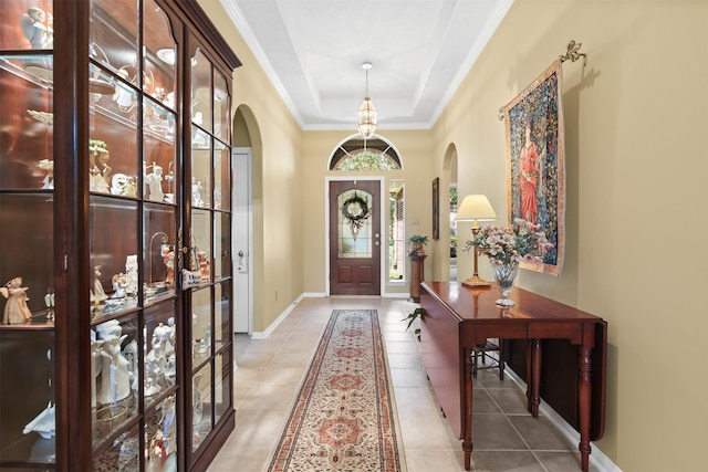 entrance foyer featuring arched walkways, baseboards, a raised ceiling, light tile patterned flooring, and ornamental molding