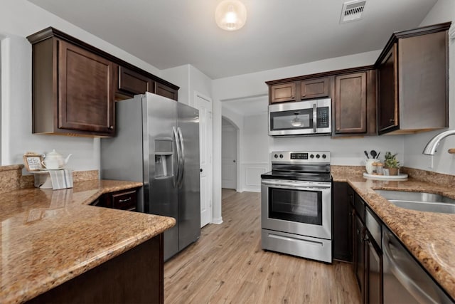 13228 Miller Ln, Willis, TX 77318 - kitchen featuring appliances with stainless steel finishes, a sink, dark brown cabinets, light wood-style flooring, and light stone countertops