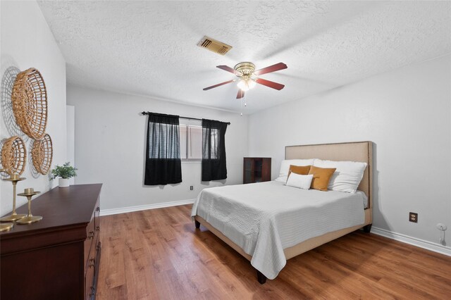 bedroom with wood finished floors, a textured ceiling, baseboards, and ceiling fan