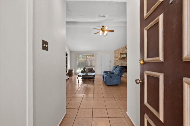foyer entrance with a ceiling fan, light tile patterned flooring, vaulted ceiling, and a fireplace