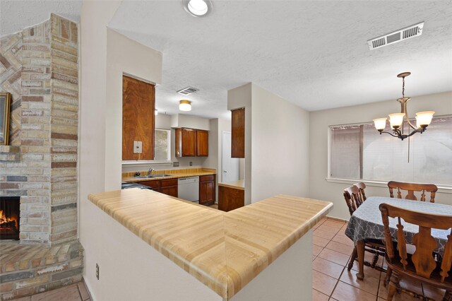 kitchen with dishwasher, a fireplace, a chandelier, light tile patterned flooring, and a textured ceiling