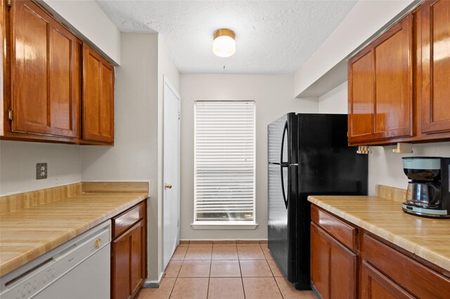 kitchen featuring white dishwasher, light countertops, brown cabinetry, freestanding refrigerator, and a textured ceiling