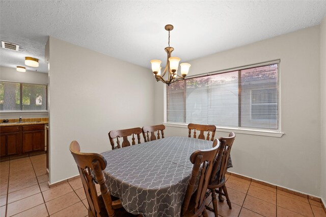 dining space with a chandelier, light tile patterned floors, baseboards, and a textured ceiling
