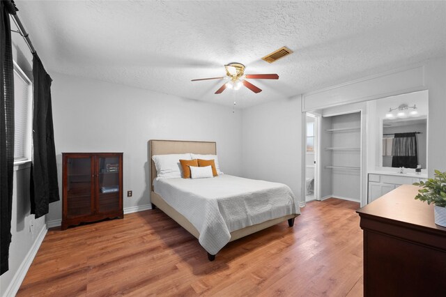 bedroom featuring light wood-type flooring, a textured ceiling, ceiling fan, and baseboards