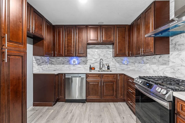 kitchen with appliances with stainless steel finishes, wall chimney exhaust hood, a sink, tasteful backsplash, and light wood-type flooring