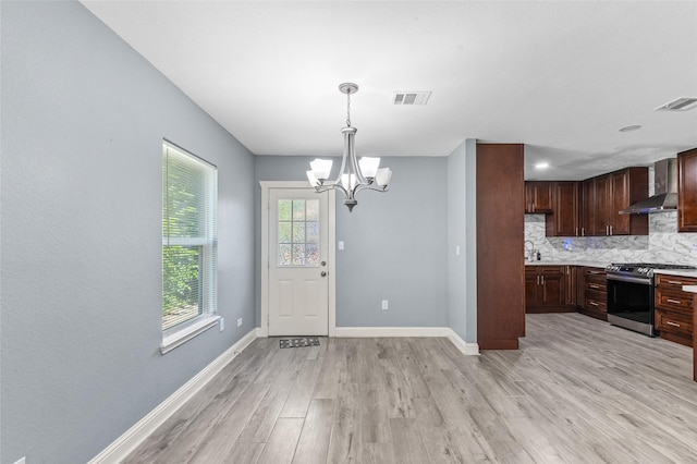 kitchen featuring stainless steel range with gas cooktop, wall chimney exhaust hood, light wood finished floors, a chandelier, and tasteful backsplash