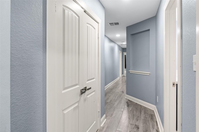 hall featuring wood finished floors, baseboards, and a textured wall