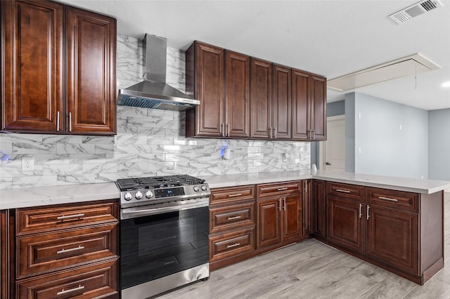 kitchen featuring wall chimney exhaust hood, stainless steel gas range oven, a peninsula, and tasteful backsplash