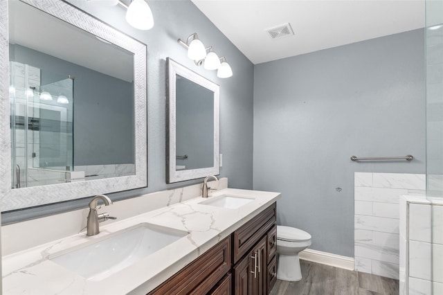 full bath with toilet, wood finished floors, a shower, double vanity, and baseboards