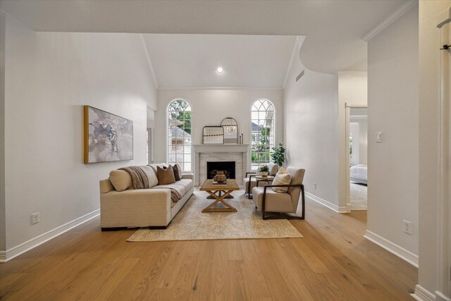 living room featuring lofted ceiling, wood finished floors, baseboards, a brick fireplace, and ornamental molding