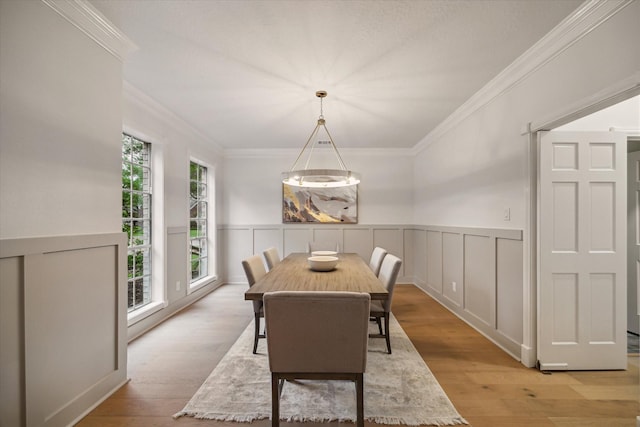 dining room featuring ornamental molding, wainscoting, light wood-type flooring, and a decorative wall