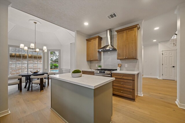 kitchen featuring wall chimney exhaust hood, stainless steel gas stove, brown cabinets, a center island, and light wood-type flooring