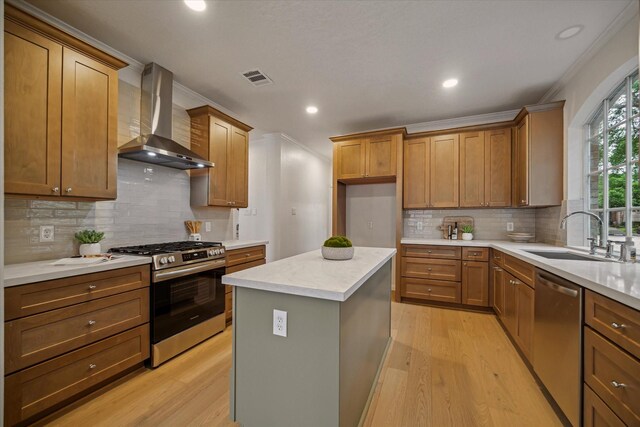 kitchen featuring stainless steel appliances, wall chimney range hood, light wood-style flooring, a sink, and recessed lighting
