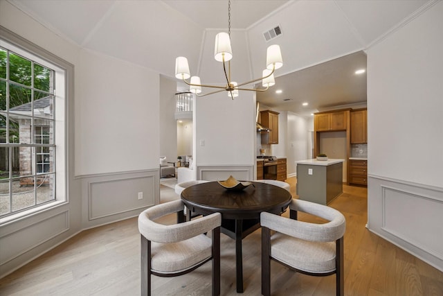dining space featuring a chandelier, light wood-type flooring, a wainscoted wall, crown molding, and a decorative wall