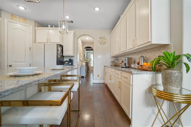 kitchen featuring freestanding refrigerator, arched walkways, decorative backsplash, dark wood finished floors, and recessed lighting