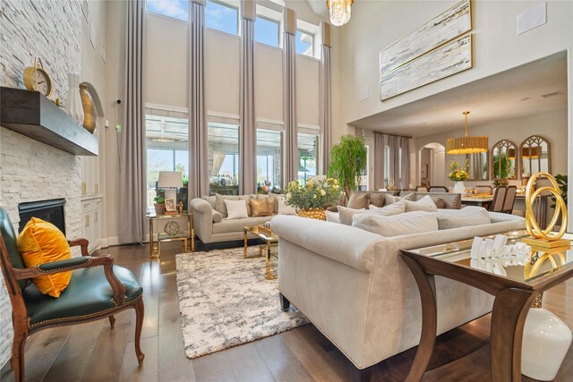living room with a high ceiling, a chandelier, a stone fireplace, dark wood-style flooring, and arched walkways