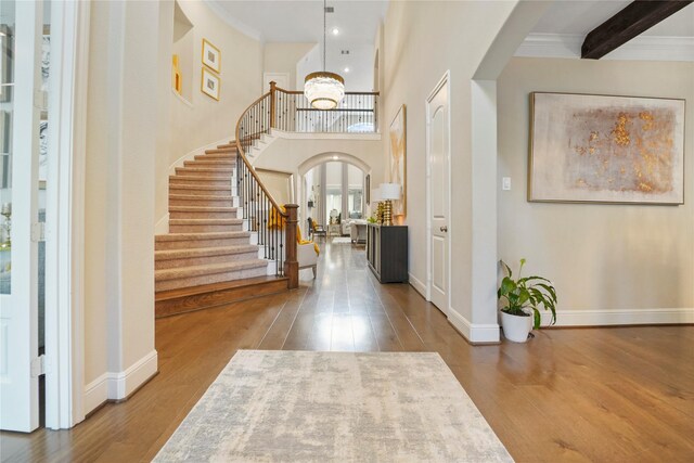 foyer with wood finished floors, arched walkways, stairs, a chandelier, and a high ceiling