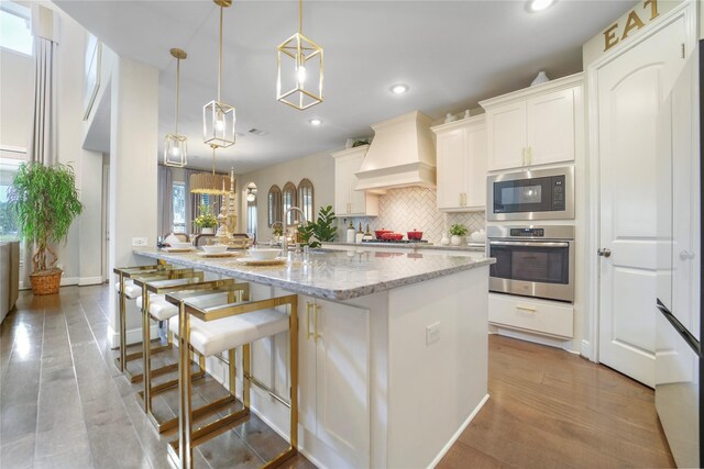 kitchen featuring appliances with stainless steel finishes, custom exhaust hood, tasteful backsplash, recessed lighting, and a center island with sink