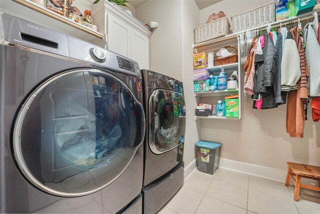 clothes washing area featuring washer and dryer, cabinet space, light tile patterned floors, and baseboards