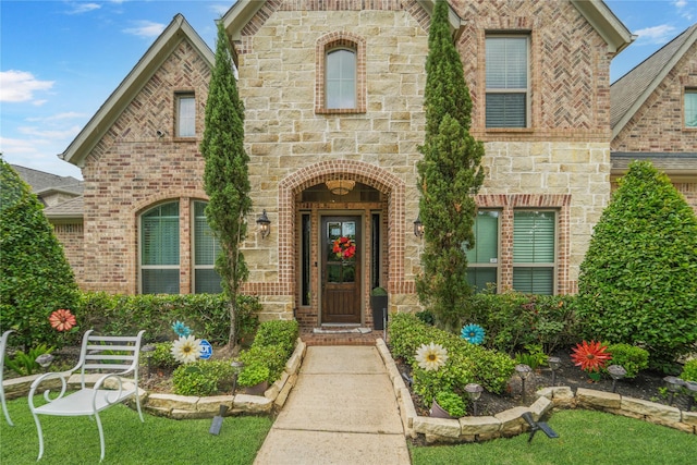 entrance to property with stone siding, brick siding, and a lawn