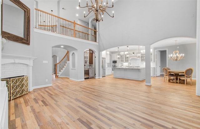 9803 White Rock Lake Trl, Cypress, TX 77433 - unfurnished living room featuring a chandelier, light wood finished floors, a high ceiling, arched walkways, and a fireplace
