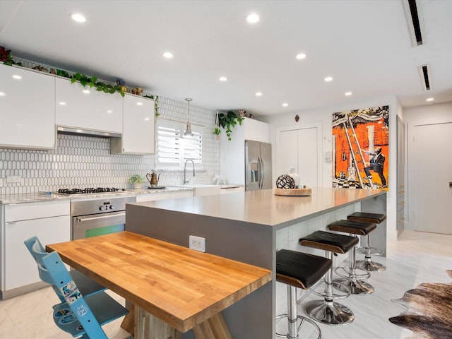 kitchen featuring stainless steel appliances, white cabinetry, tasteful backsplash, a breakfast bar, and recessed lighting