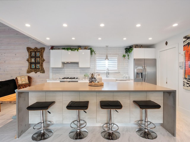 kitchen with stainless steel fridge, white cabinetry, a breakfast bar area, light countertops, and recessed lighting