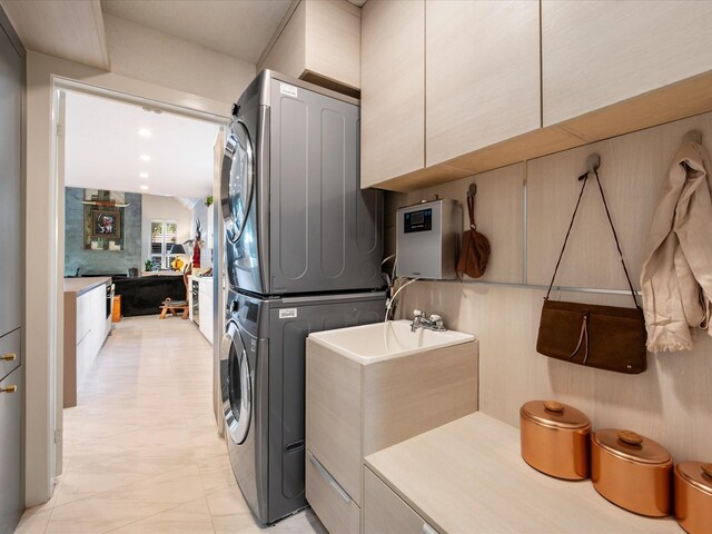 laundry room featuring stacked washer / drying machine, cabinet space, and light marble finish flooring