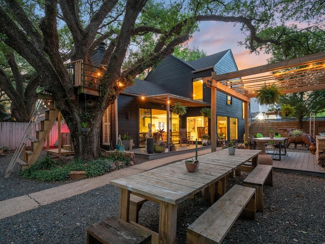 back of property at dusk with outdoor dining space, fence, a pergola, and a deck