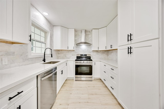 kitchen featuring wall chimney exhaust hood, stainless steel appliances, a sink, backsplash, and light wood-style flooring