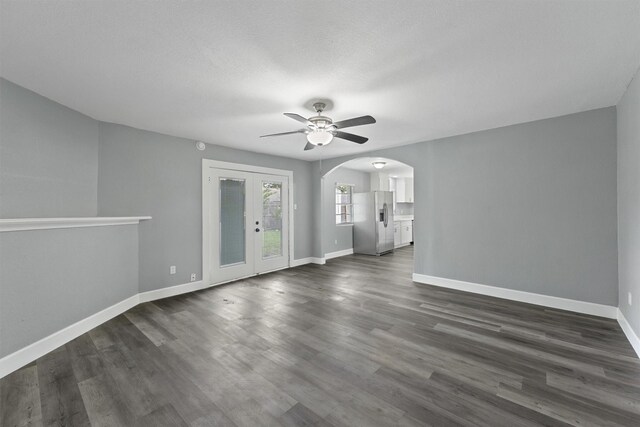 empty room featuring ceiling fan, arched walkways, baseboards, and dark wood finished floors