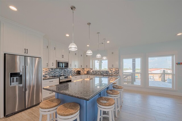 kitchen featuring stainless steel appliances, light wood-type flooring, backsplash, a breakfast bar area, and a kitchen island