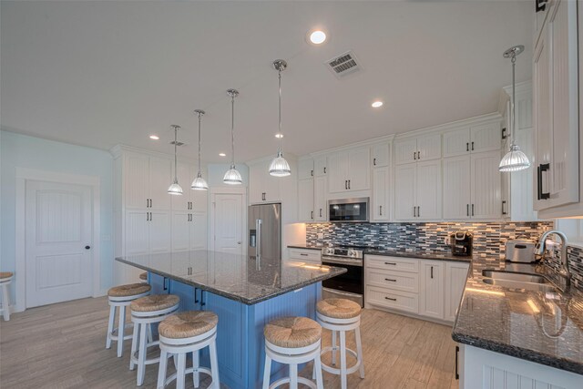 kitchen featuring appliances with stainless steel finishes, a sink, light wood-style floors, backsplash, and white cabinetry