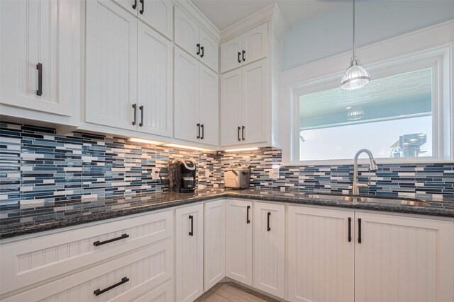 kitchen with a sink, backsplash, white cabinets, dark stone countertops, and decorative light fixtures