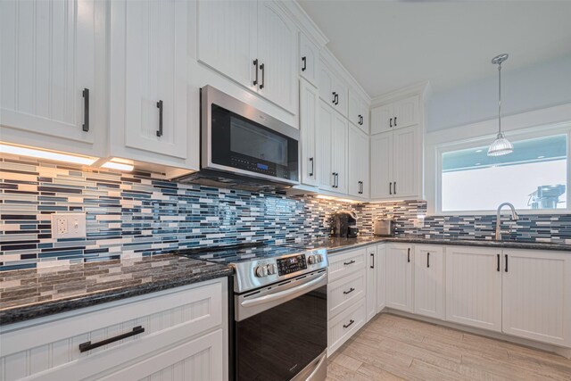 kitchen with stainless steel appliances, a sink, tasteful backsplash, white cabinetry, and dark stone counters