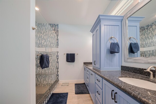 full bath featuring walk in shower, double vanity, baseboards, and wood finished floors