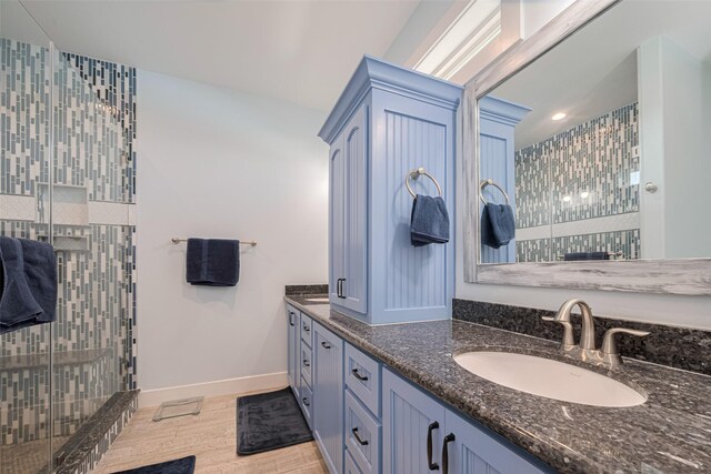 full bath featuring double vanity, tiled shower, wood finished floors, baseboards, and recessed lighting
