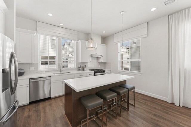 kitchen with appliances with stainless steel finishes, a sink, a kitchen bar, dark wood finished floors, and recessed lighting