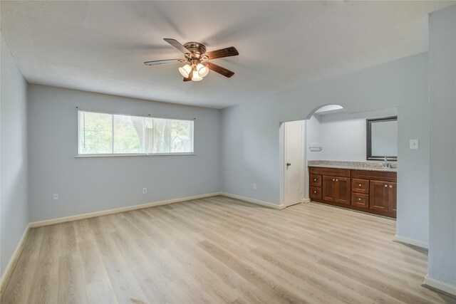 unfurnished bedroom featuring light wood finished floors, baseboards, ensuite bathroom, and a sink