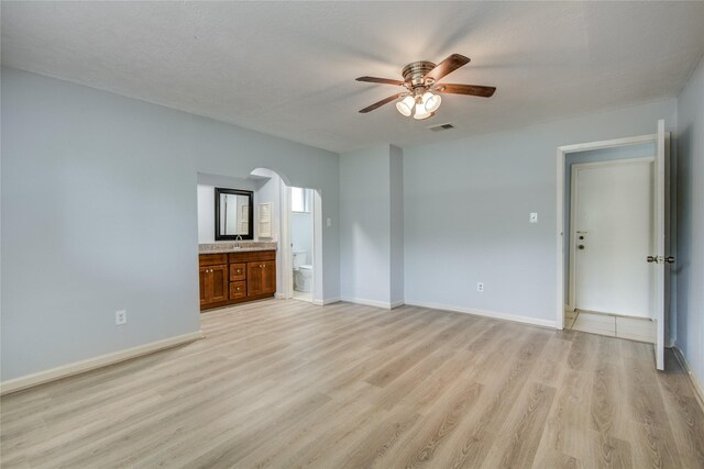 unfurnished room with ceiling fan, light wood-type flooring, arched walkways, baseboards, and a sink