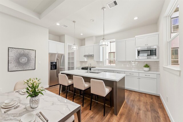 kitchen with stainless steel appliances, backsplash, a breakfast bar area, an island with sink, and recessed lighting