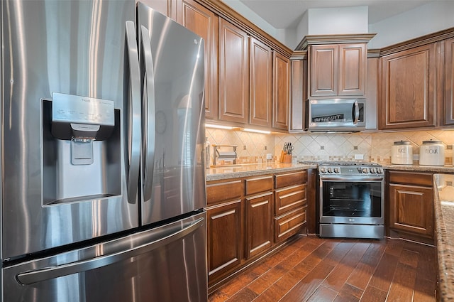 kitchen featuring stainless steel appliances, dark wood-style flooring, decorative backsplash, light stone countertops, and brown cabinets