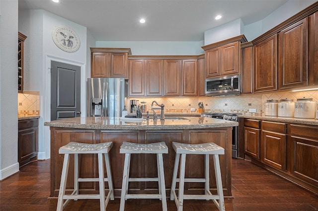 kitchen with appliances with stainless steel finishes, tasteful backsplash, a sink, a center island with sink, and a kitchen bar