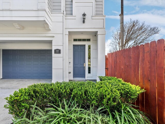 view of exterior entry with fence, a garage, and driveway