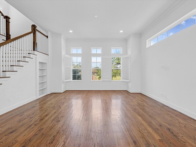 unfurnished living room featuring wood-type flooring, stairs, baseboards, built in features, and crown molding