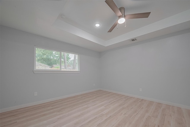 empty room with light wood-type flooring, baseboards, a raised ceiling, recessed lighting, and ceiling fan