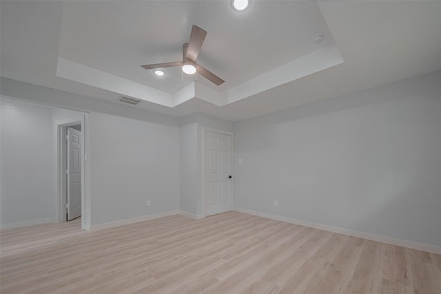 empty room featuring a raised ceiling, light wood-type flooring, a ceiling fan, baseboards, and recessed lighting