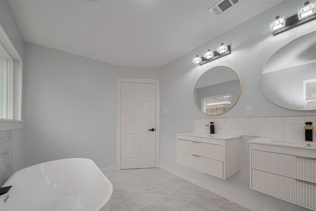 bathroom with marble look tiles, two vanities, and a freestanding tub