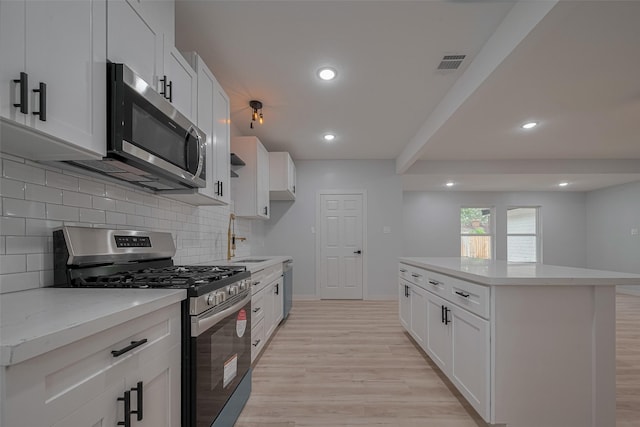 kitchen with appliances with stainless steel finishes, a sink, light wood-style flooring, decorative backsplash, and recessed lighting